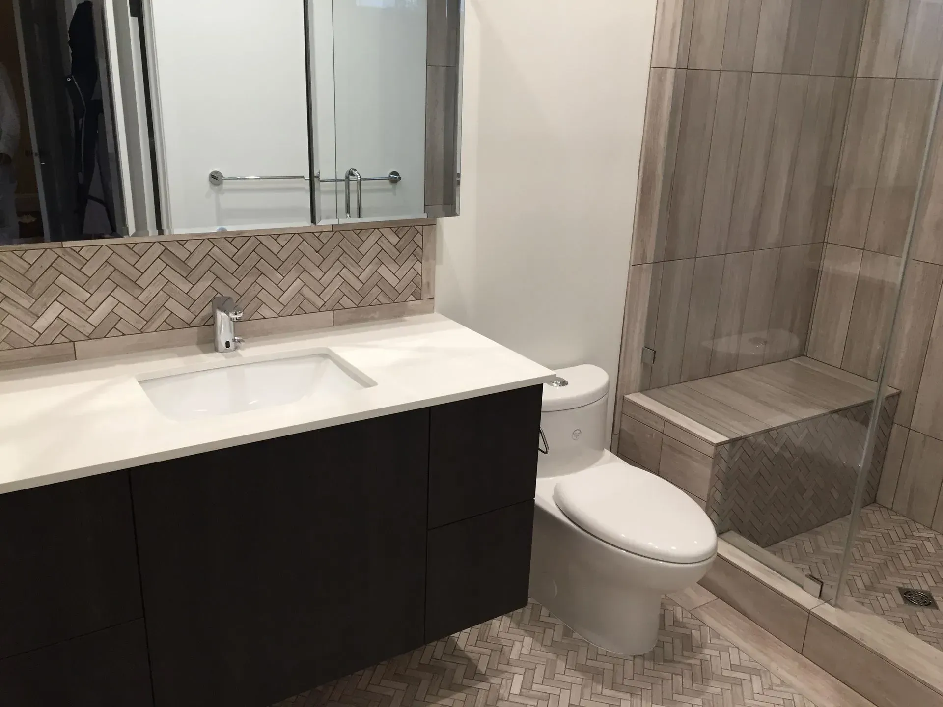 Modern bathroom with white vanity, dark cabinets, toilet, and tiled shower area