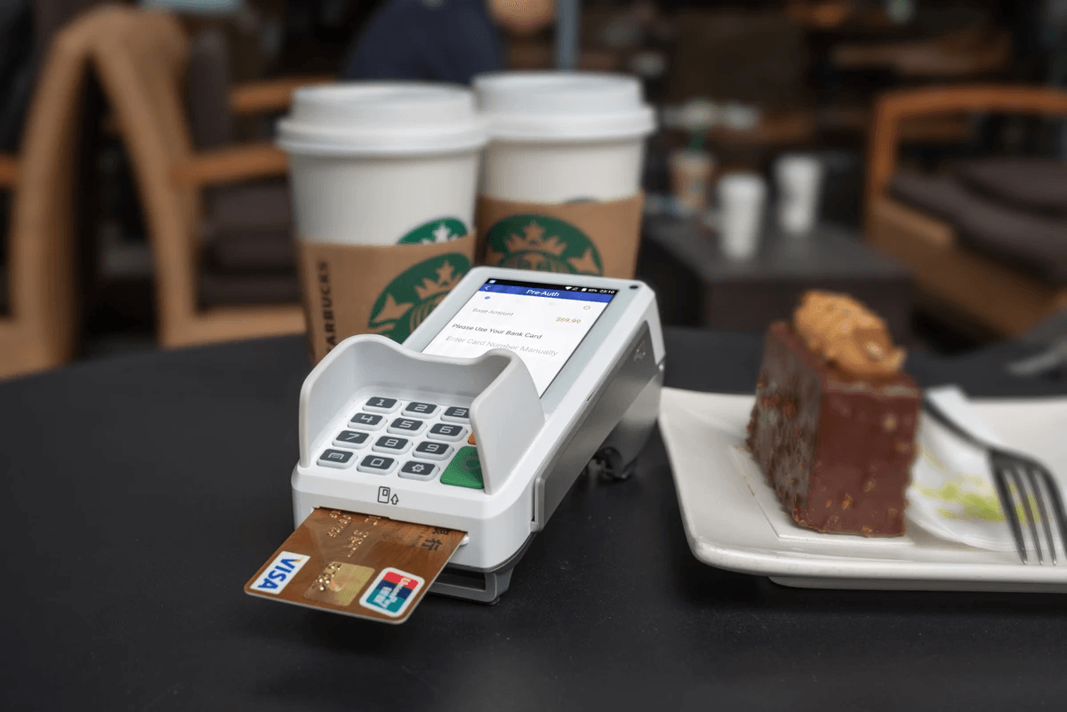 A credit card reader is sitting on a table next to a plate of food.