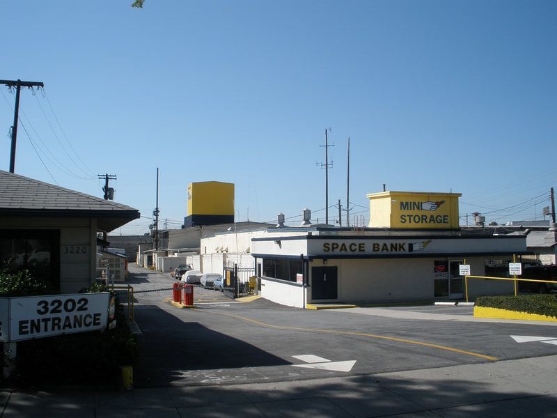 Entrance to Space Banks storage facility. White and yellow buildings, clear sky. Sign reads 