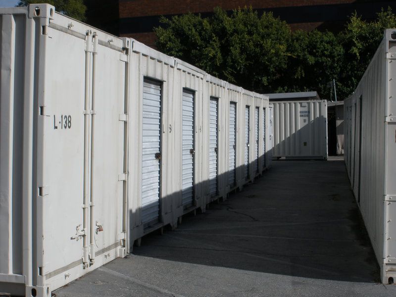 Row of white storage units with doors and a concrete pathway.