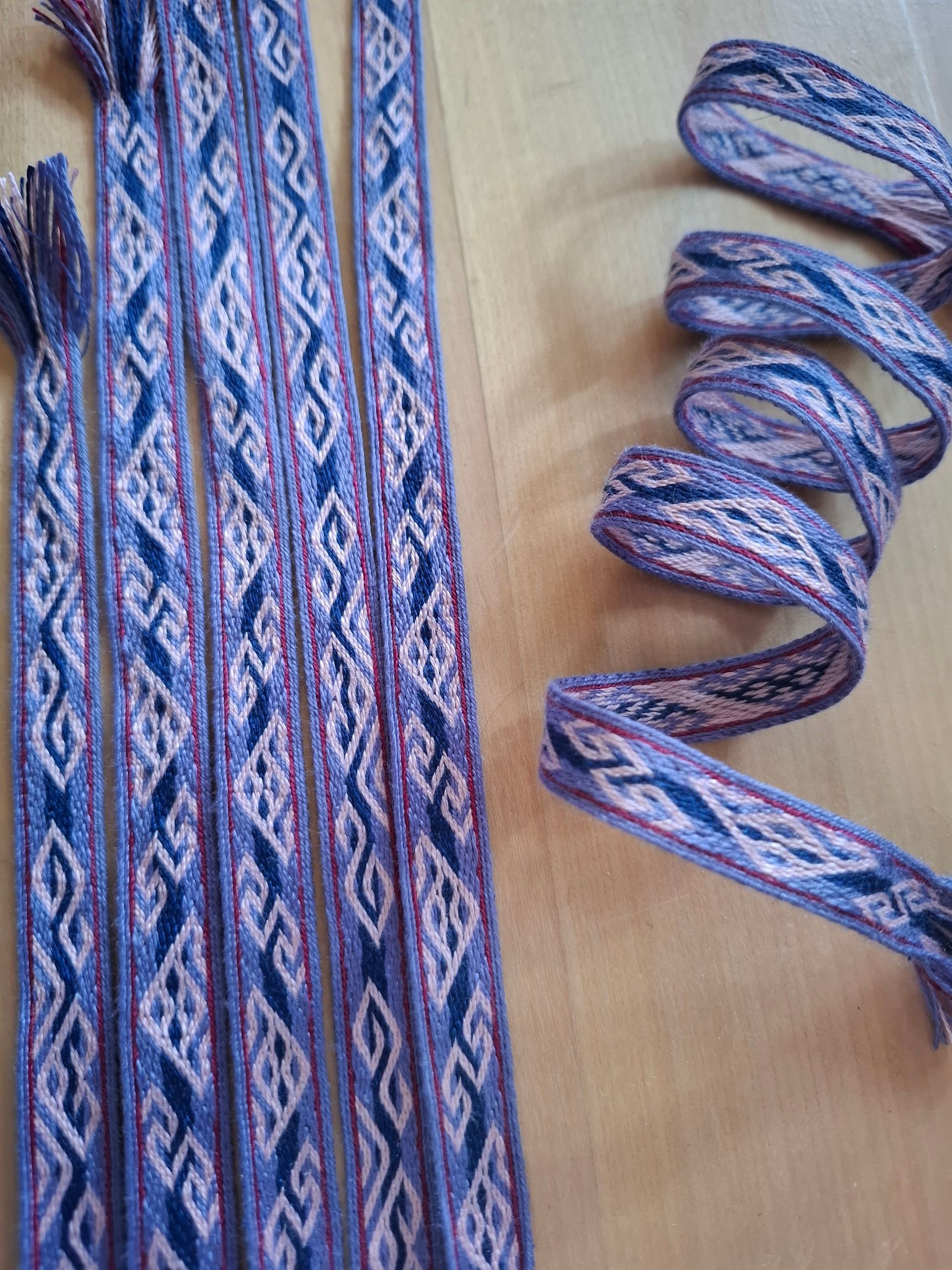 Geweven linten met paarse, roze en crèmekleurige patronen, gerangschikt op een houten oppervlak.