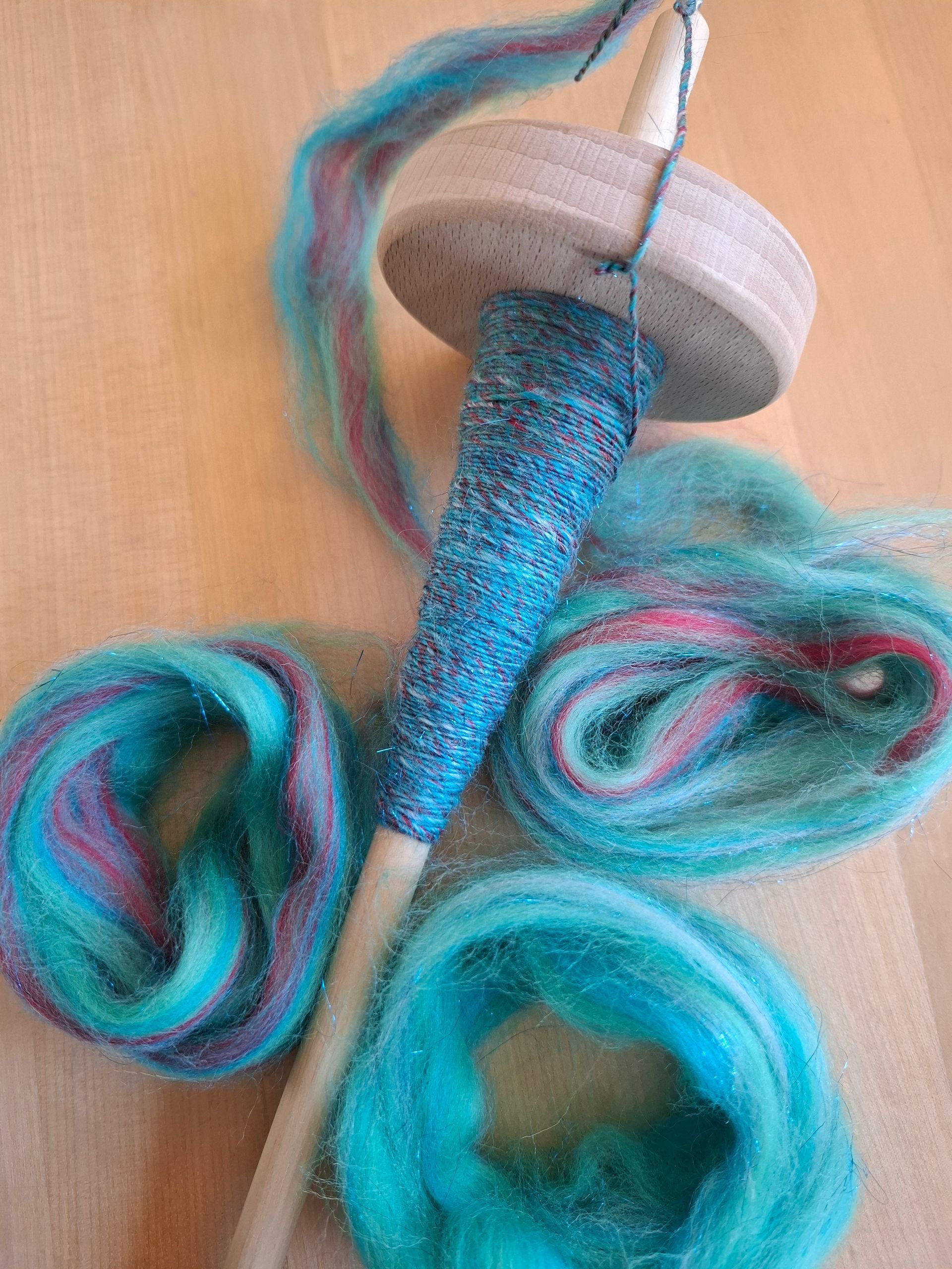 Een spinnewiel met turquoise garen en vezels, op hout gezet.