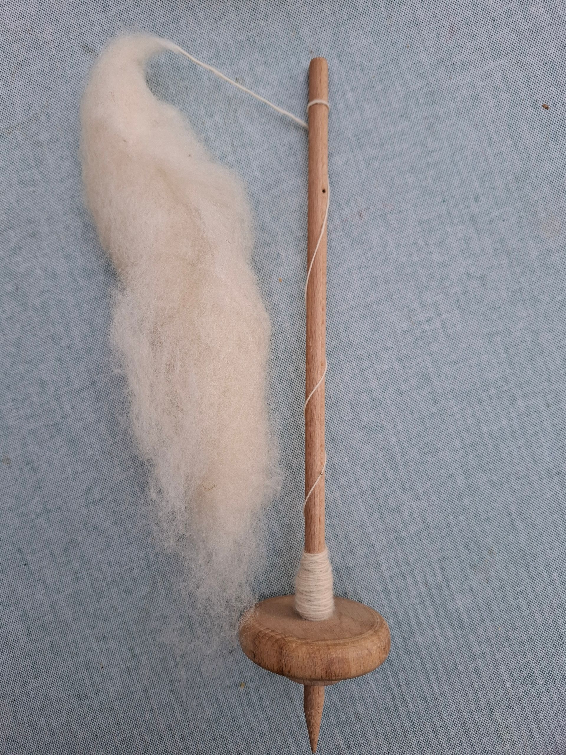 Spindel van hout met witte vezels, rustend op een blauw oppervlak.
