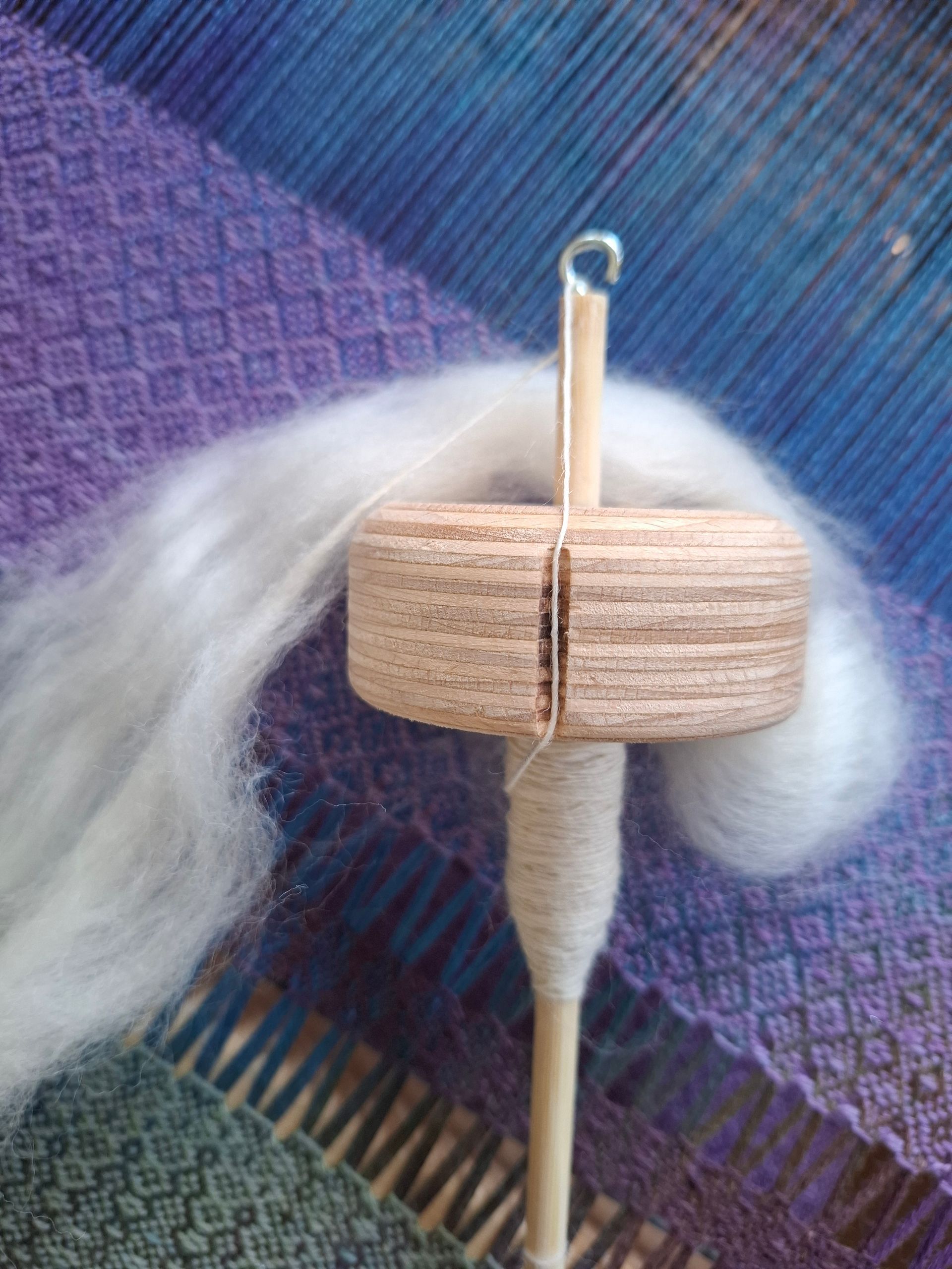 In zijn hand houdt hij een houten spinnewiel vast, waaraan wit garen is gesponnen. Bovenaan is onafgewerkte wol bevestigd.