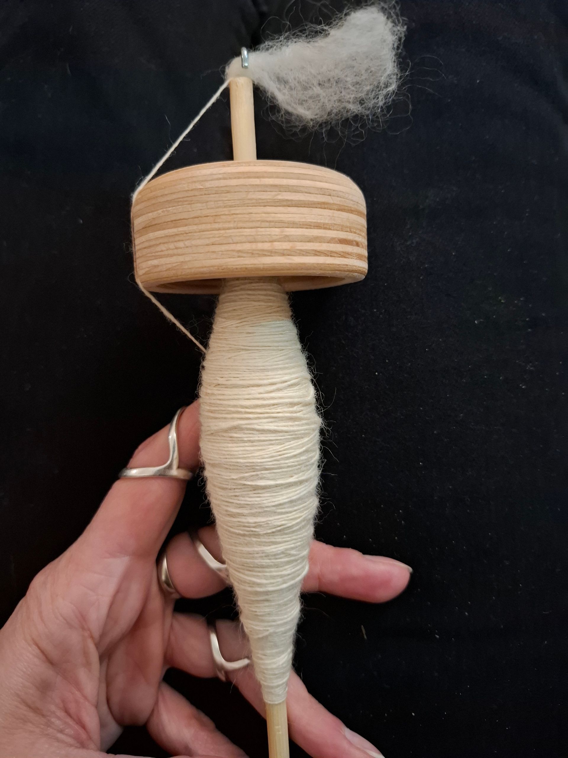 In zijn hand houdt hij een houten spinnewiel vast, waaraan wit garen is gesponnen. Bovenaan is onafgewerkte wol bevestigd.