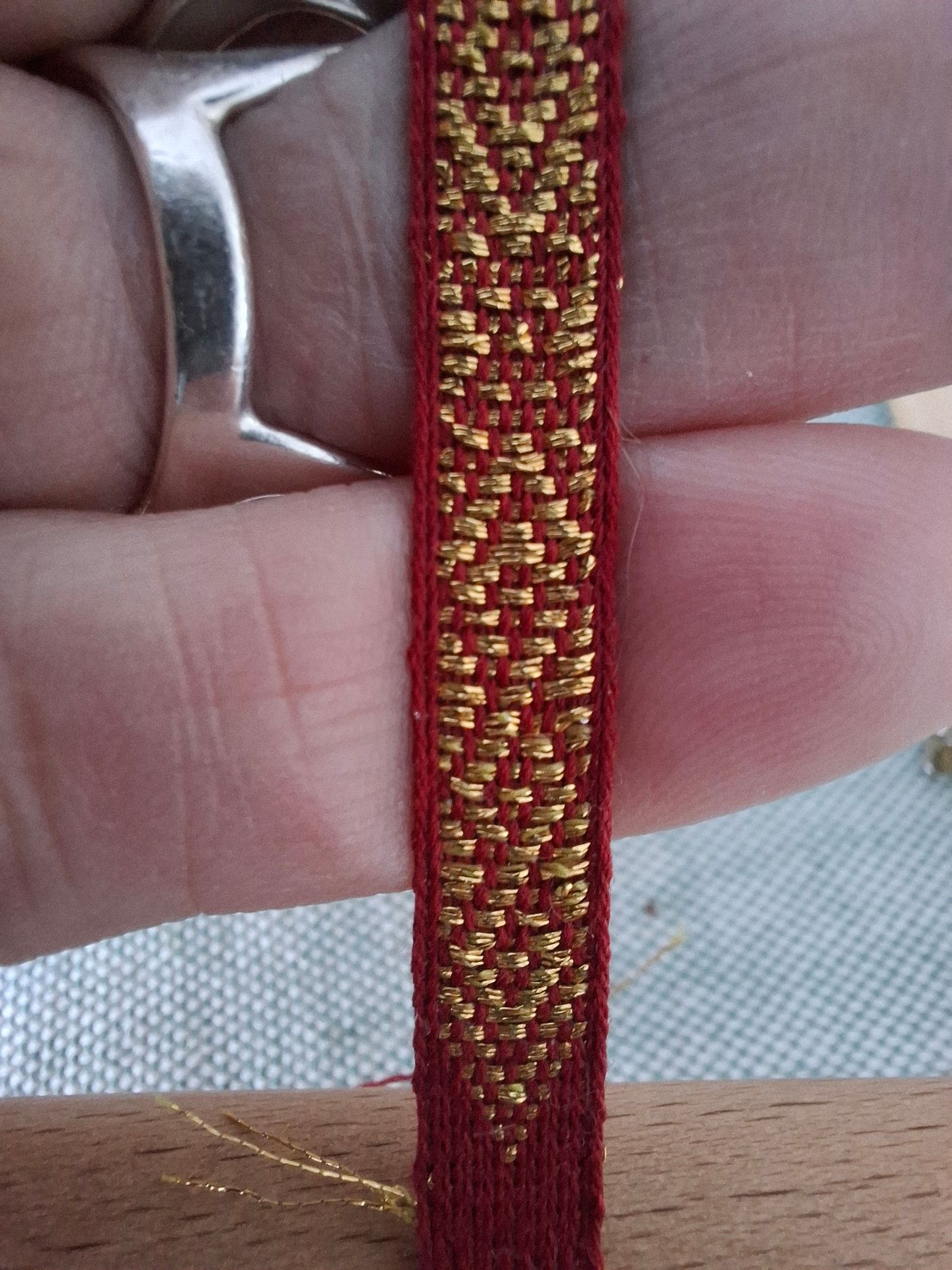 Een persoon met een zilveren ring houdt een rood en goudkleurig patroon vast.