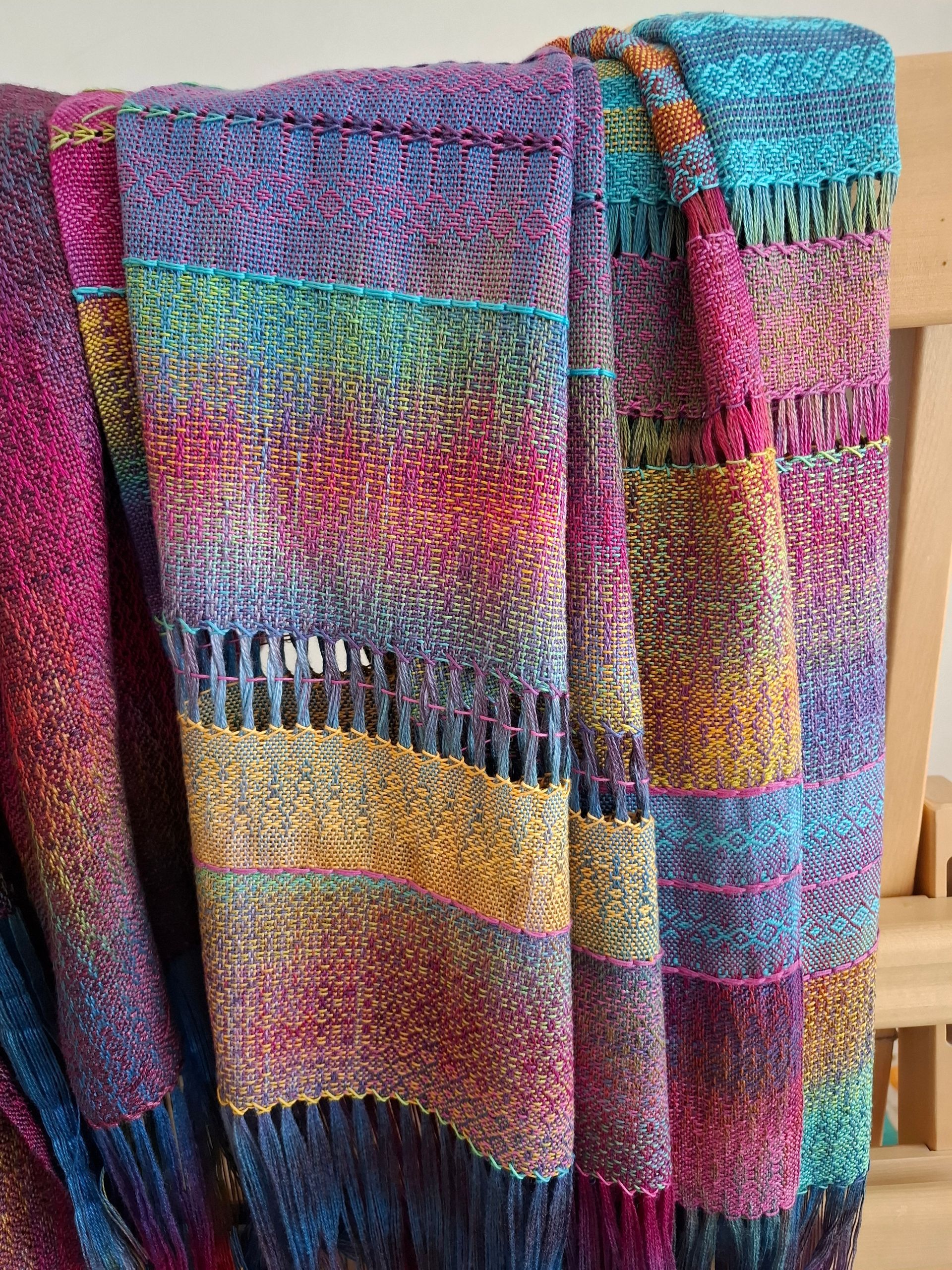 Kleurrijke geweven deken gedrapeerd over een houten stoel. Met banden in felle kleuren en franjes aan de randen.