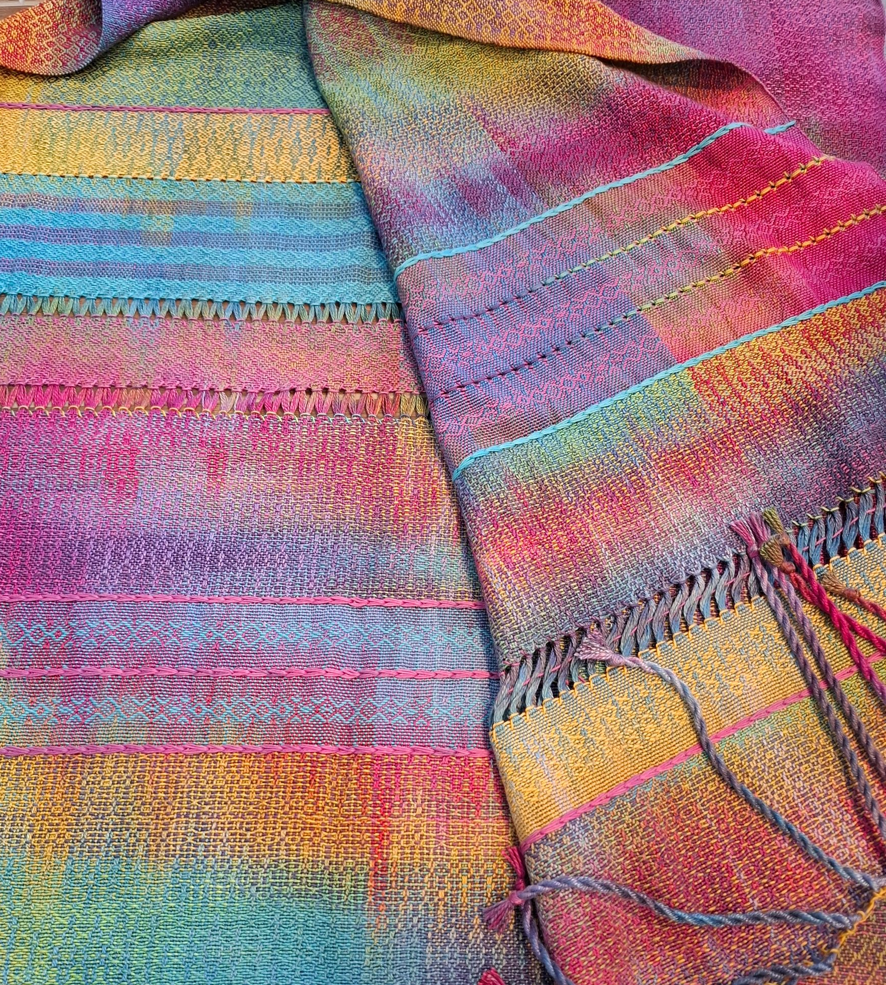 Kleurrijke geweven deken gedrapeerd over een houten stoel. Met banden in felle kleuren en franjes aan de randen.