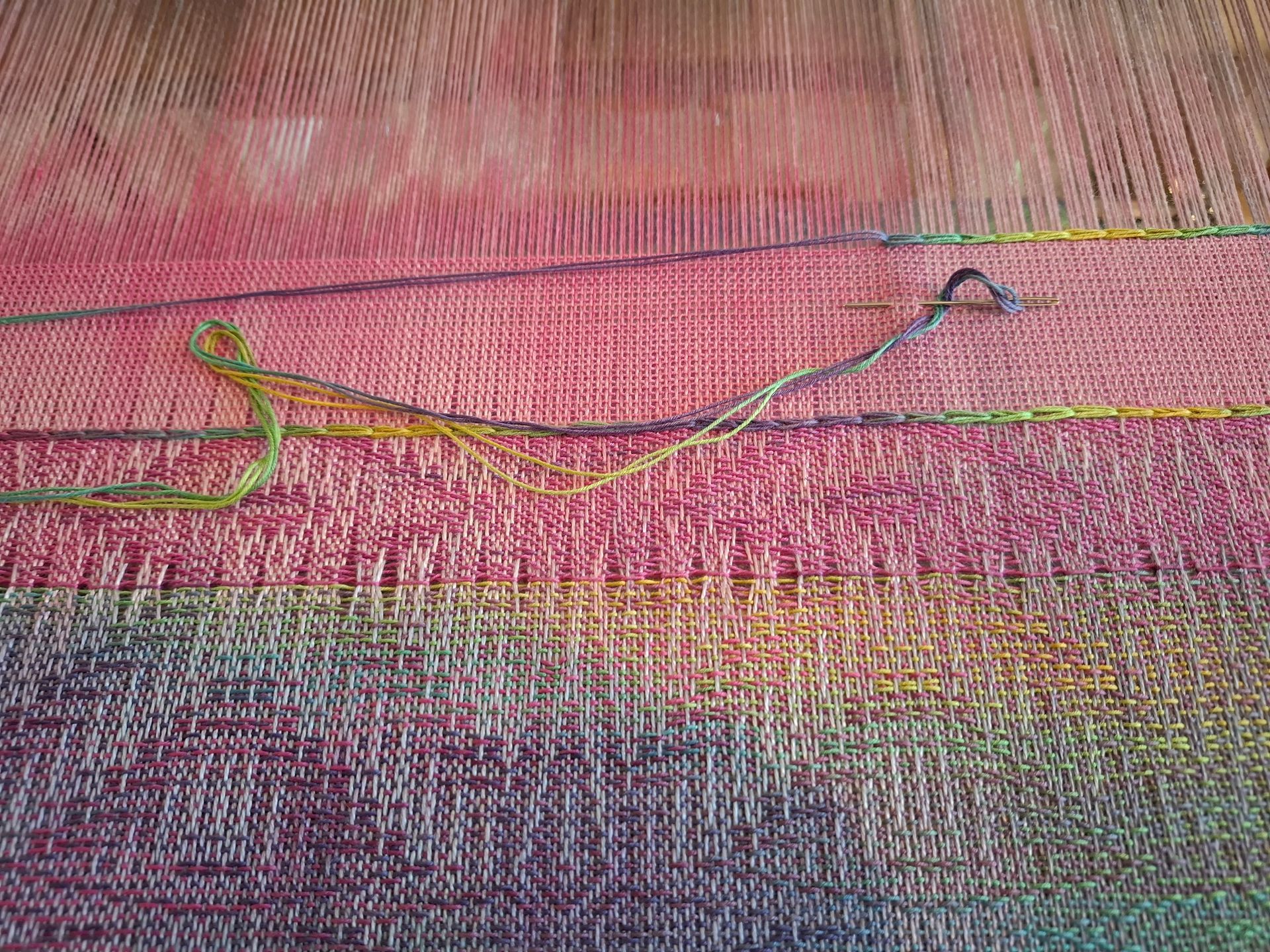 Weefgetouw met blauwe en bruine draden, een naald en groen garen zichtbaar.