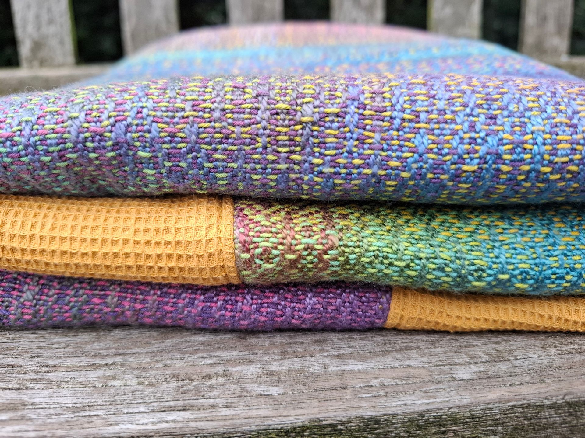 Kleurrijk textielkunstwerk met een mosterdgele rand op een houten bank.