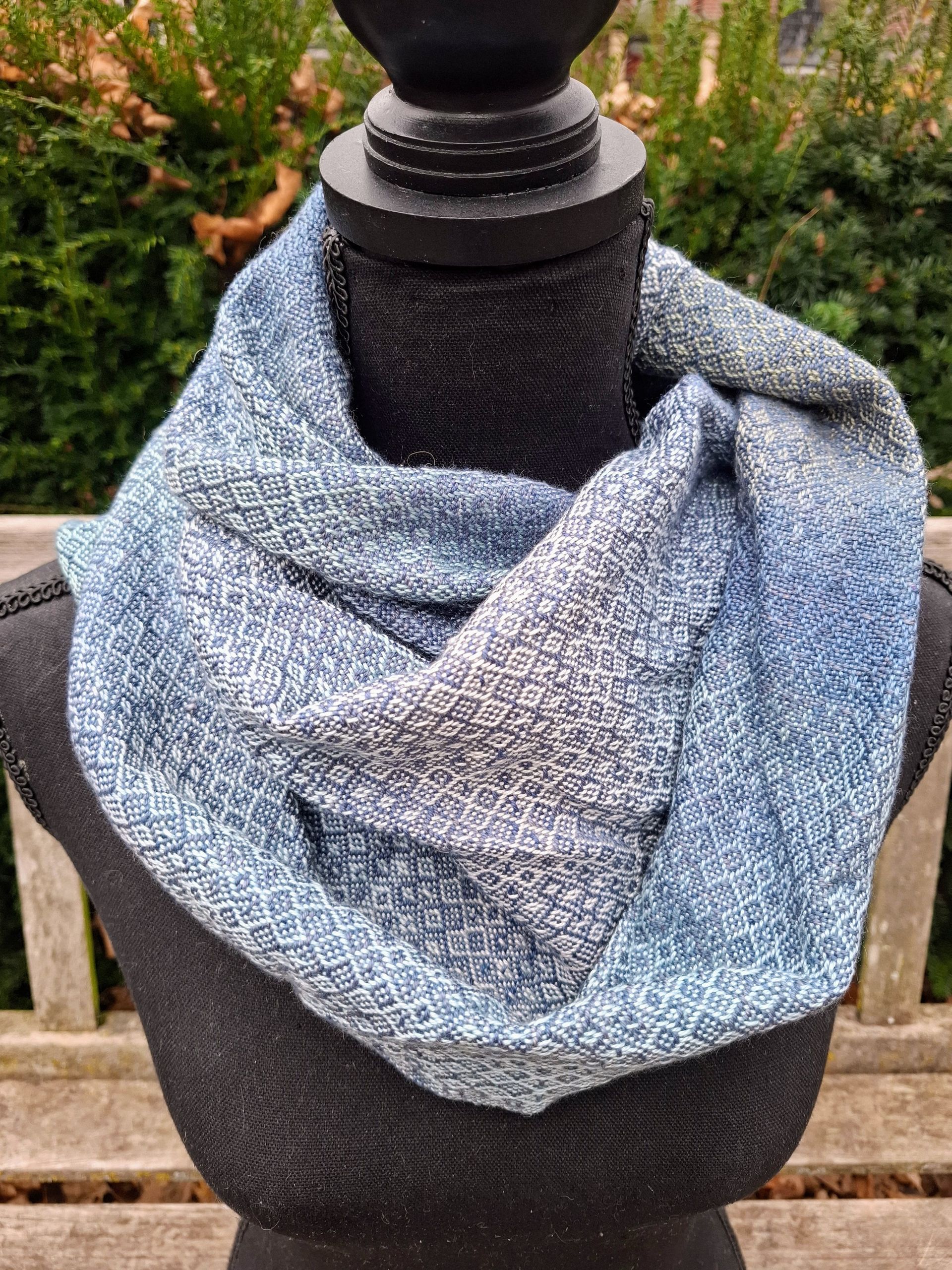 Blauwe en grijze gebreide infinity-sjaal op een zwarte mannequin.