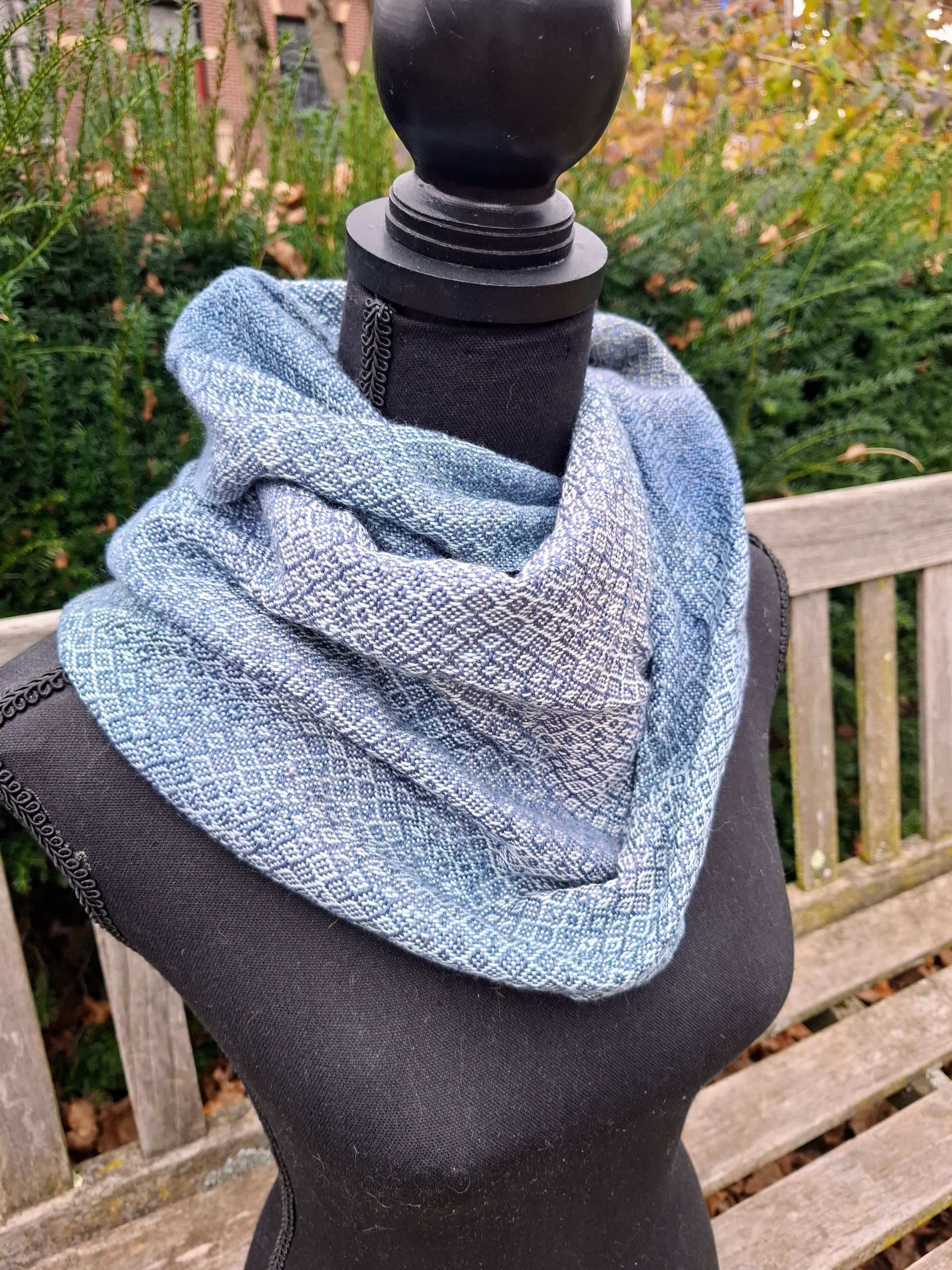 Blauwe en grijze gebreide infinity-sjaal op een zwarte mannequin.