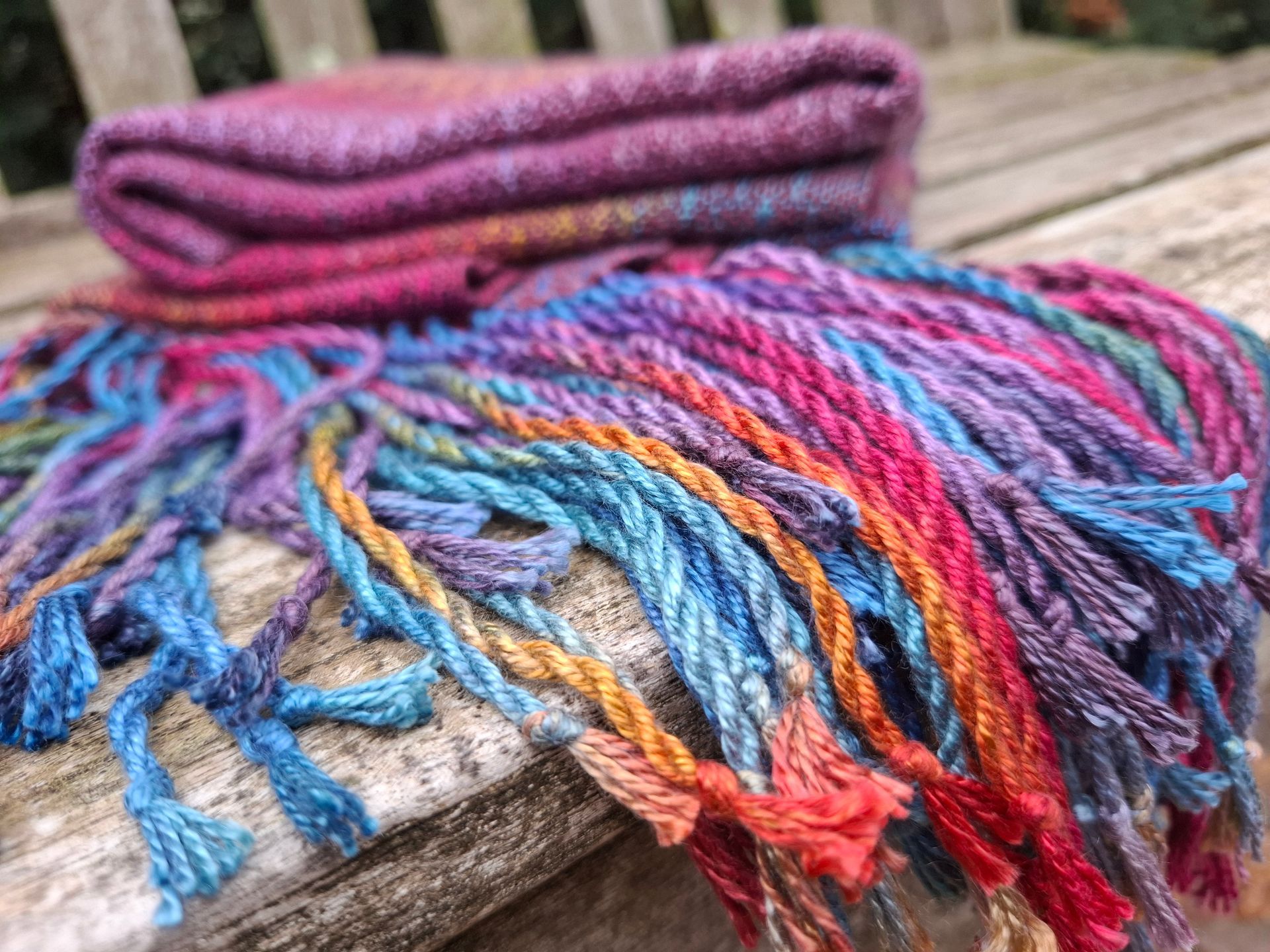 Kleurrijke sjaal met franjes, gevouwen op een houten ondergrond. Verschillende tinten blauw, paars en oranje.