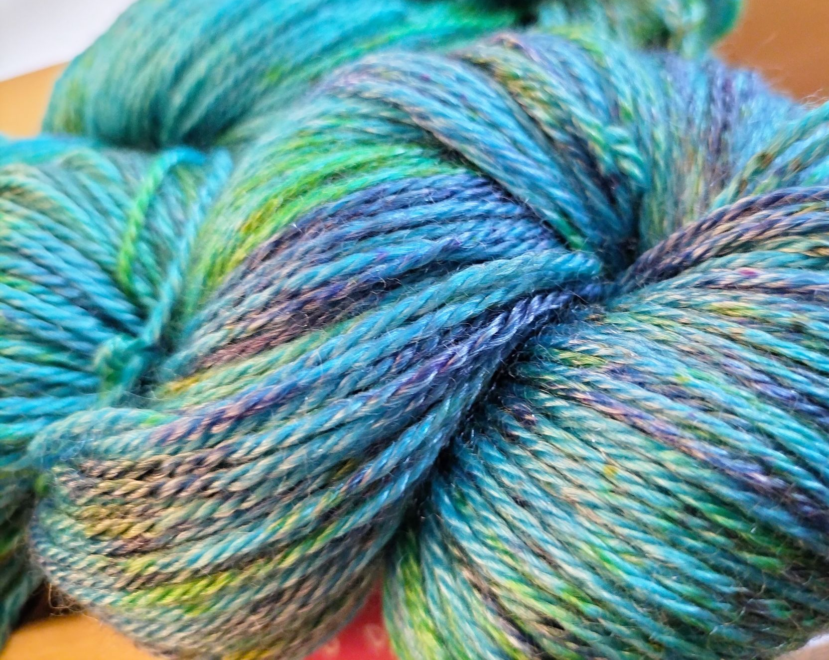 Close-up van een streng handgeverfd garen in tinten blauw, blauwgroen, groen en paars.