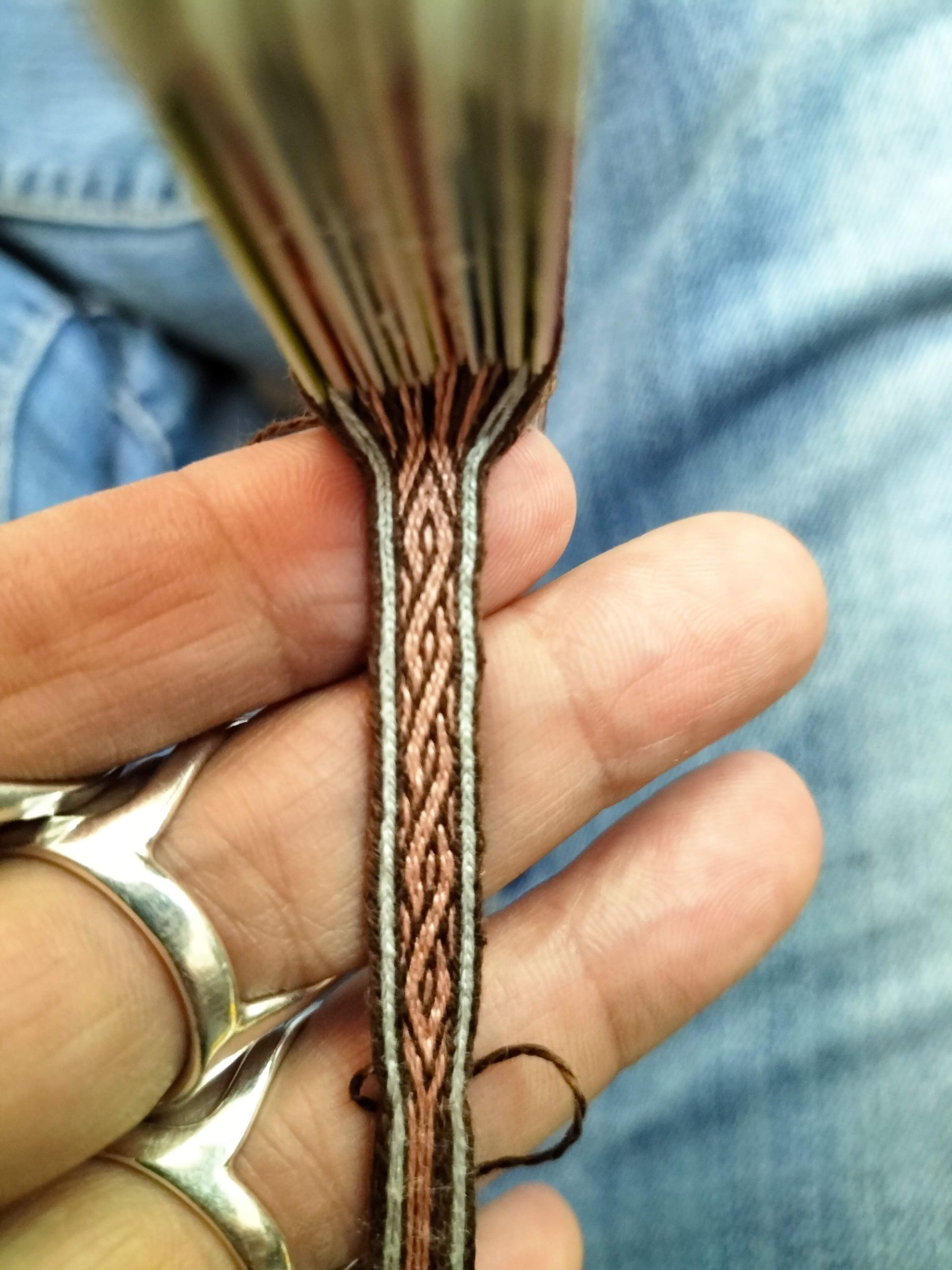 Hand houdt een gevlochten vlecht vast met bruine, bronzen en zilveren draden, schaar zichtbaar.