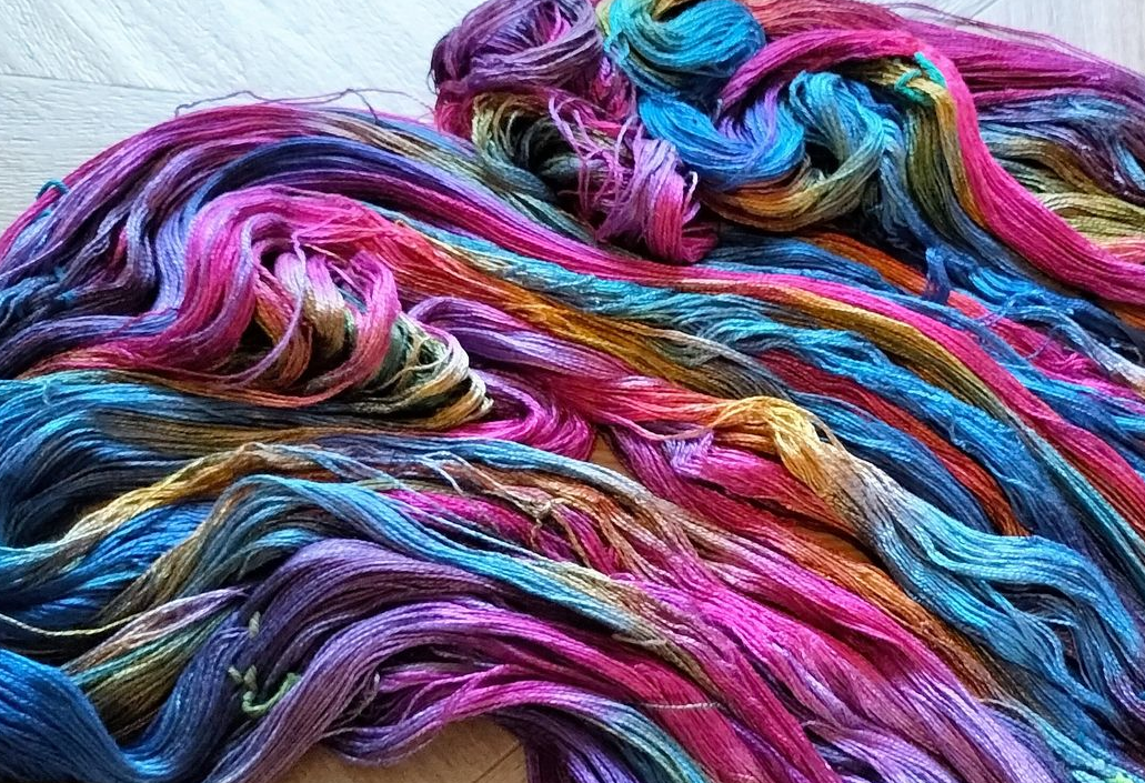 Kleurrijke, met de hand geverfde zijden draden in de kleuren roze, blauw, geel en paars, gerangschikt in een werveling.