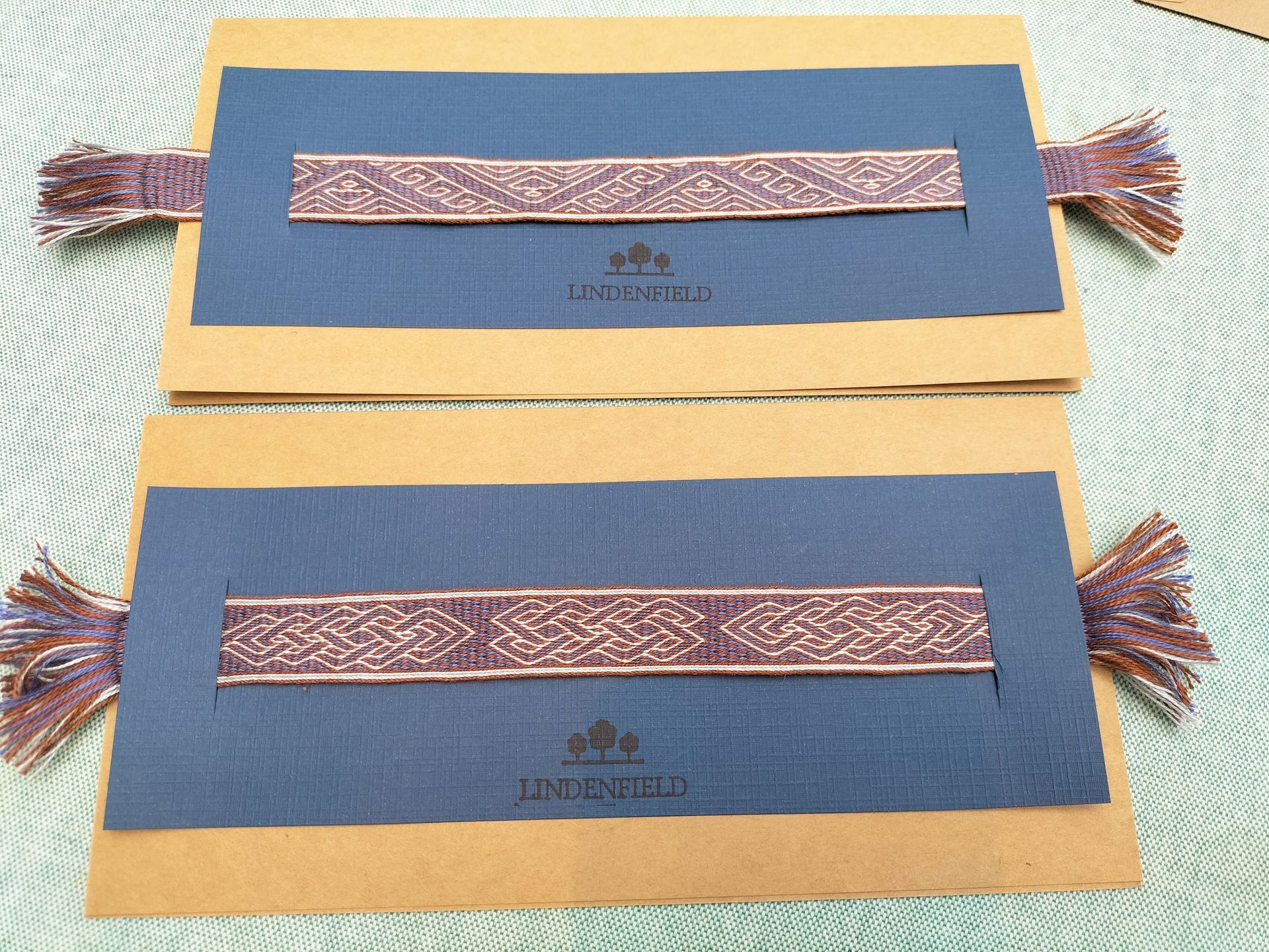 Twee stoffen banden met gedetailleerde patronen, paars op blauwe kaarten met franje.