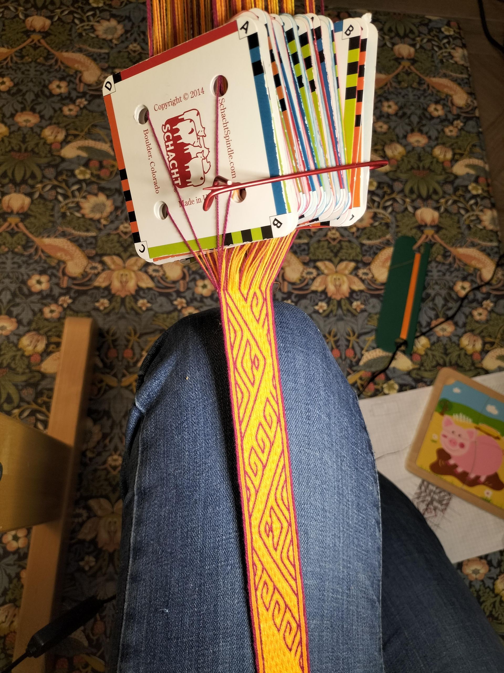 Persoon weeft een kleurrijke band met een patroon met behulp van een kaartweeftechniek. De kaarten worden boven de band gehouden, de draden zijn zichtbaar.