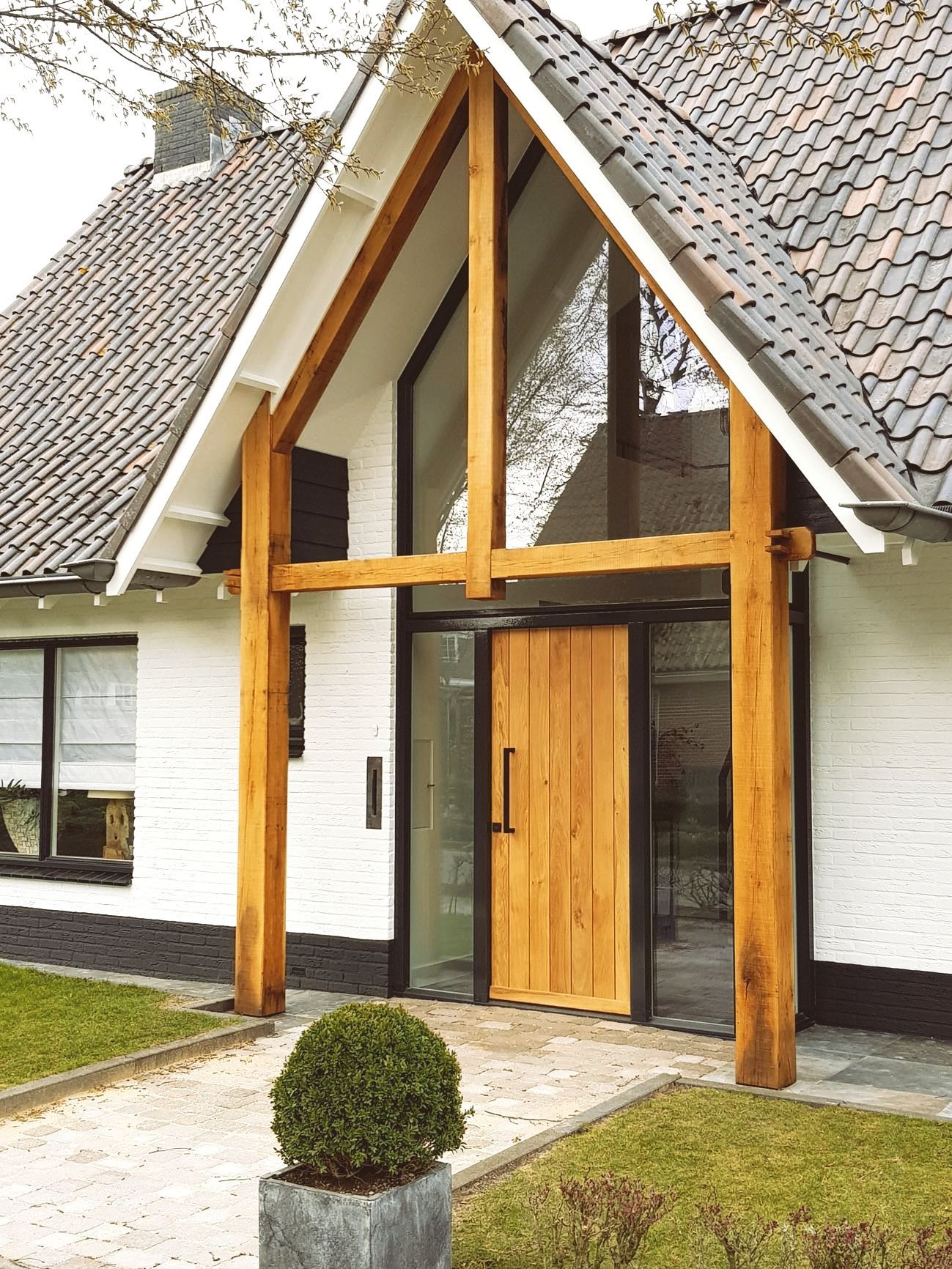 De ingang van het witte huis heeft houten balken, glazen deuren en een kleine struik.