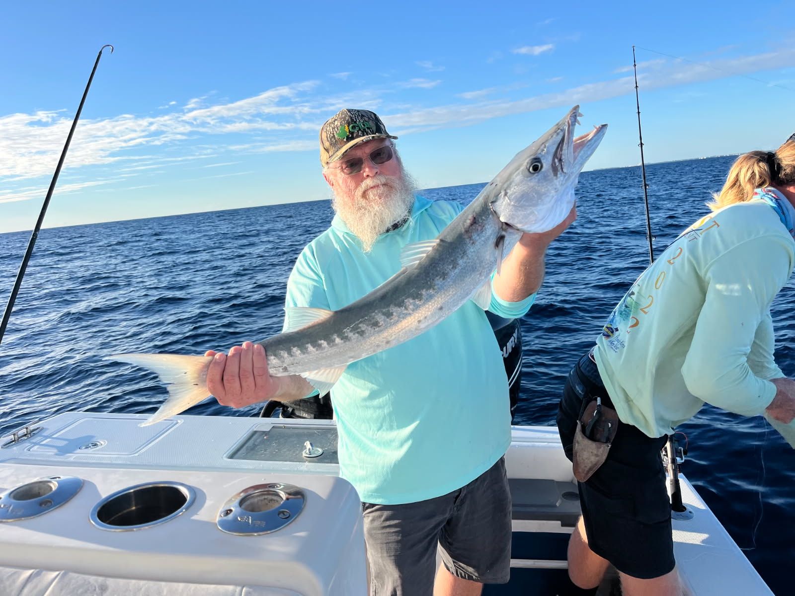 Man on boat holds up a barracuda fish with ocean and blue sky in background.