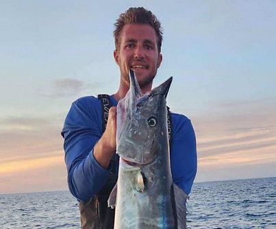 Man holding a large, blue fish with a pointed bill on a boat. Sky and ocean in background.