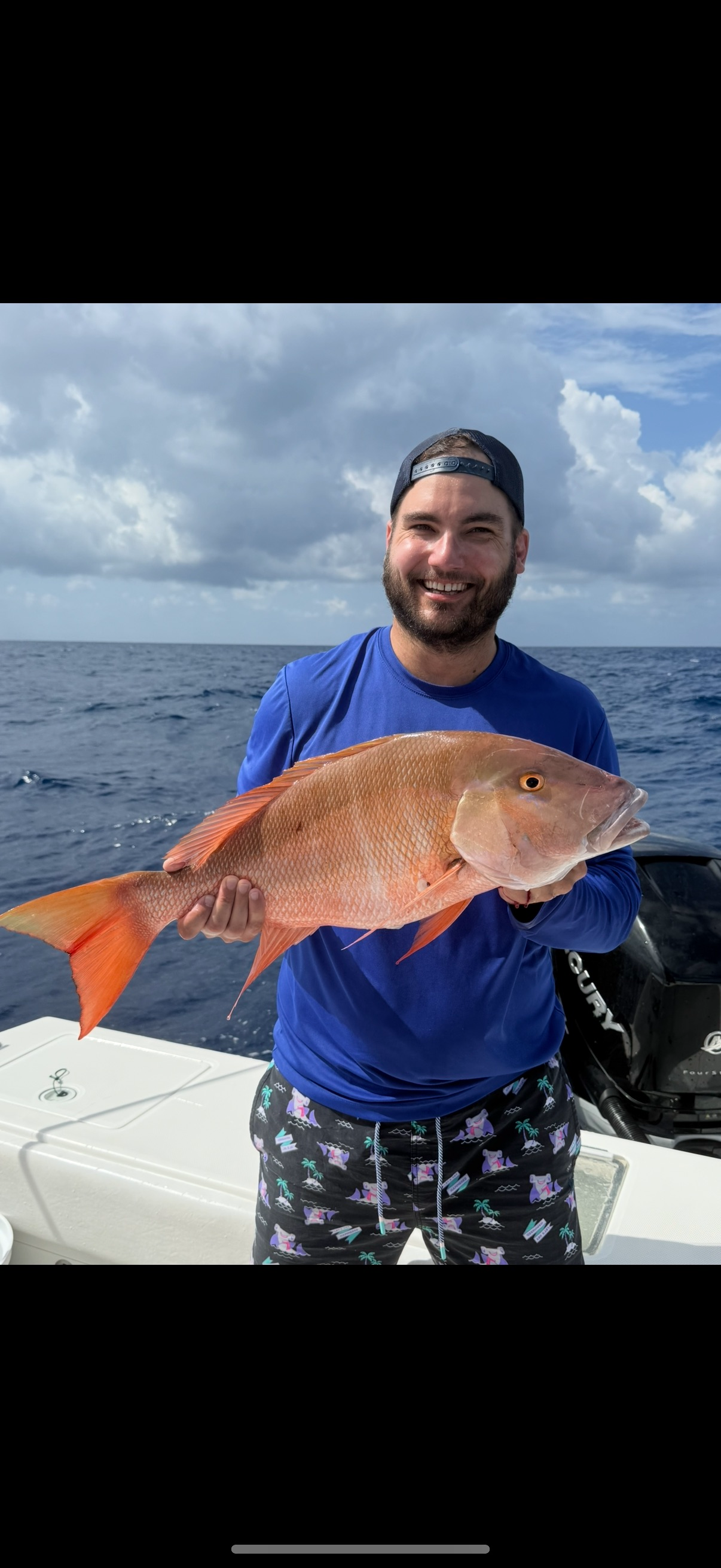 Man holding a large, blue fish with a pointed bill on a boat. Sky and ocean in background.