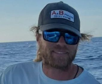 Man wearing sunglasses and a fishing hat, smiling on a boat at sea.