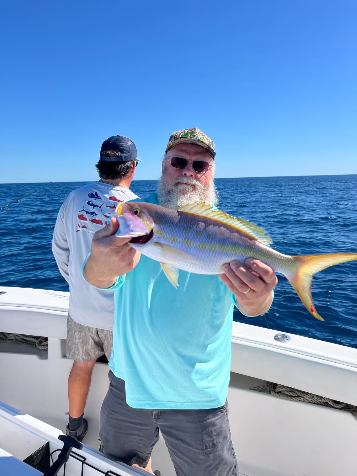 Man on boat holds up a yellowtail snapper, blue sky and water in background.
