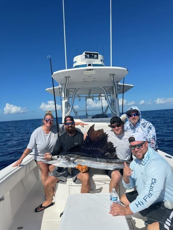 Group on boat holding large sailfish; sunny day on the water.