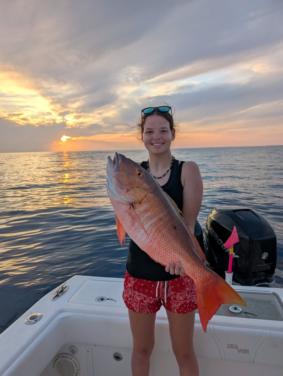 Woman holding a large red fish on a boat at sunset.