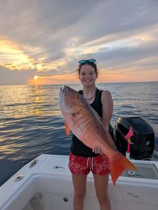 Woman holding a large red fish on a boat at sunset.