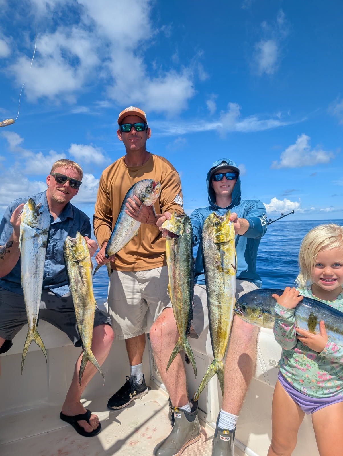Four people on a boat holding up freshly caught mahi-mahi fish on a sunny day.