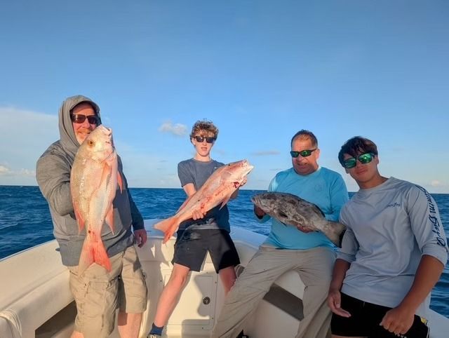 Four people on a boat holding fish. Blue water and sky. Sunny day.