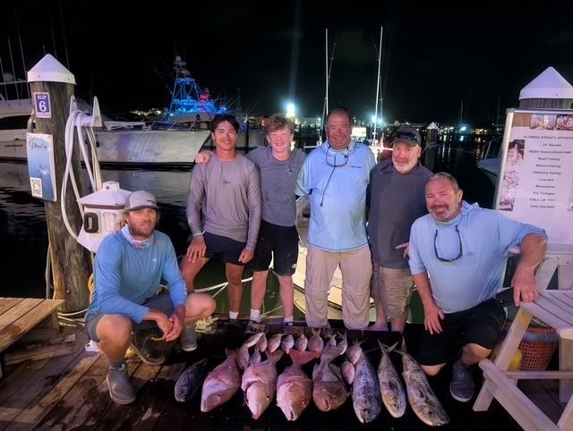 Group of people with fish catch at a dock at night.