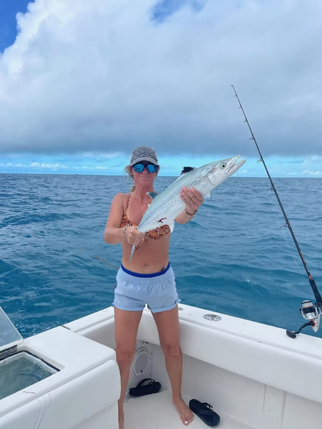 Woman on boat, holding a fish; ocean background.