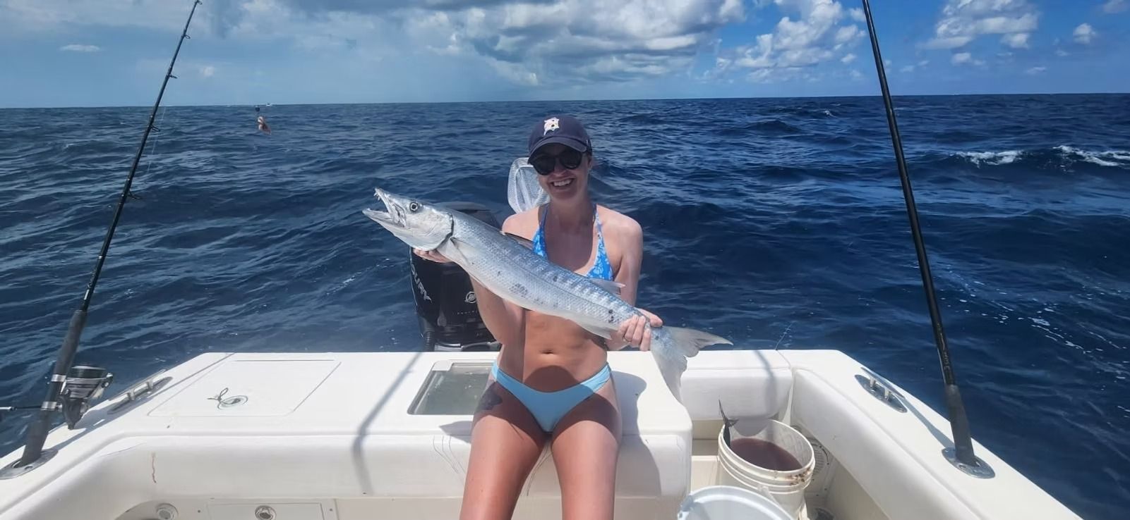 Woman on a boat holding a fish she caught, blue ocean and sky in the background.