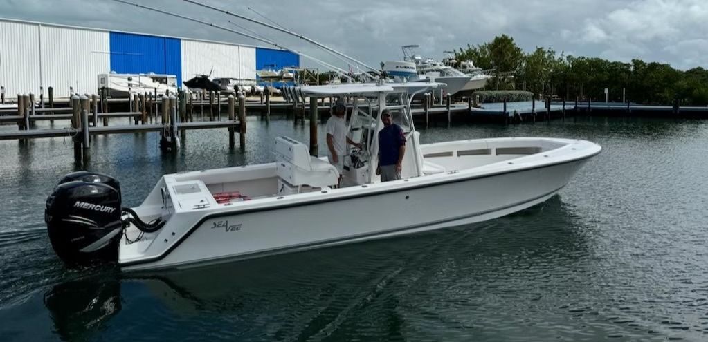 White boat with people on board moves through the water near docks and a building with a blue facade.
