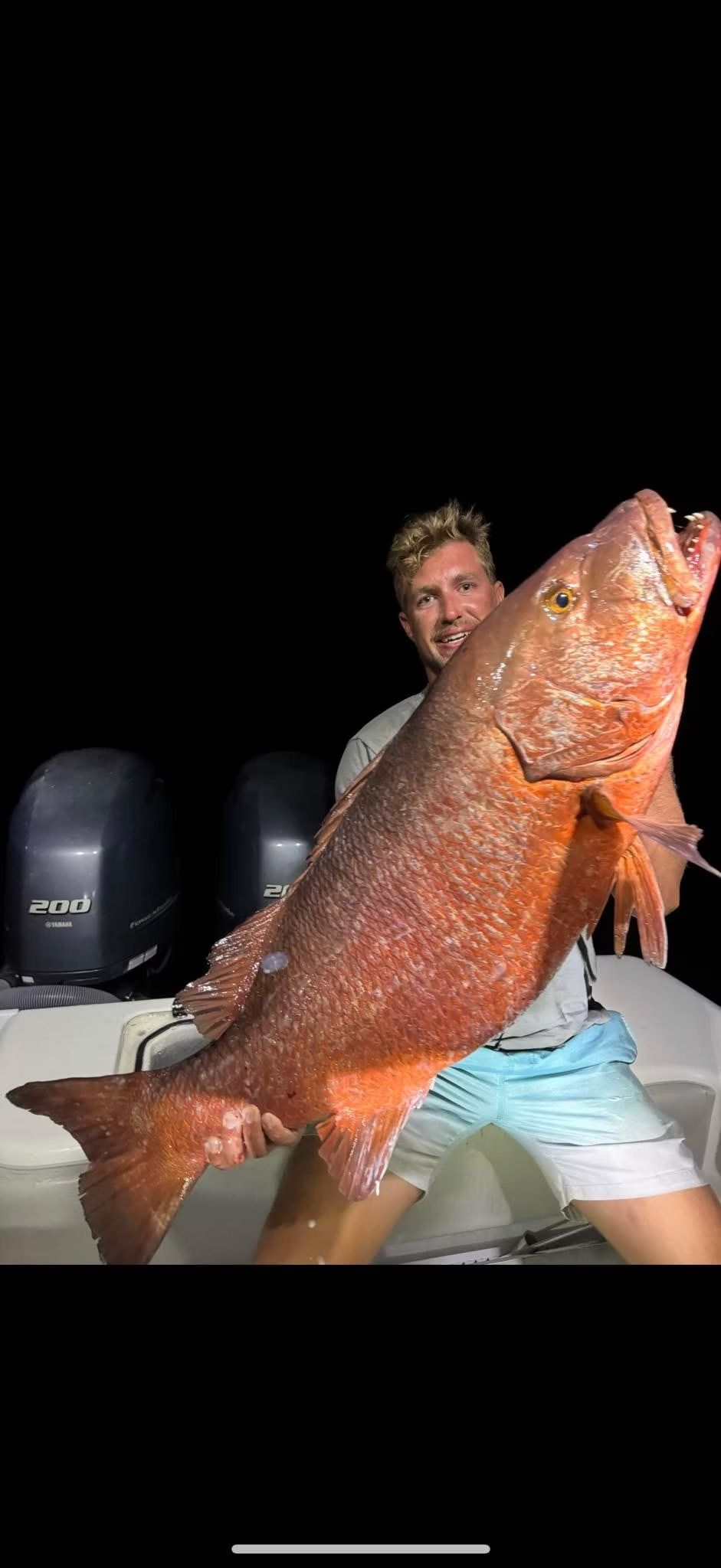 A person holding a large red fish on a boat at night.
