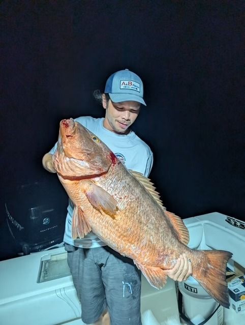 Man holding a large, reddish-brown fish on a boat at night.