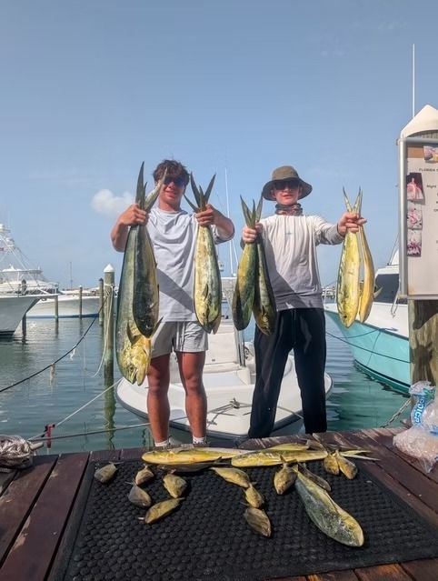 Two people holding up caught fish at a dock, with several more fish on the ground.