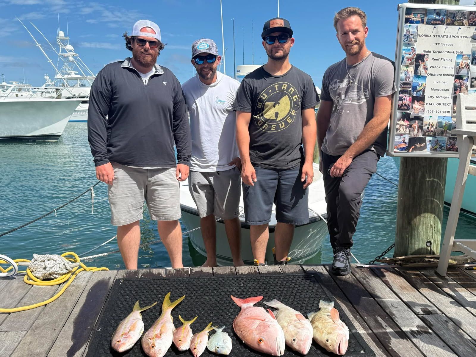 Four people stand on a dock, posing with caught fish. Sunny day.