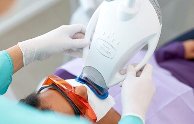 Megan Carvill Oral Hygienist is whitening a patient's teeth with a machine.
