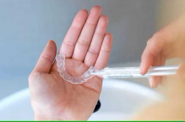 A person holds a teeth whitening tray and a syringe in their hand.