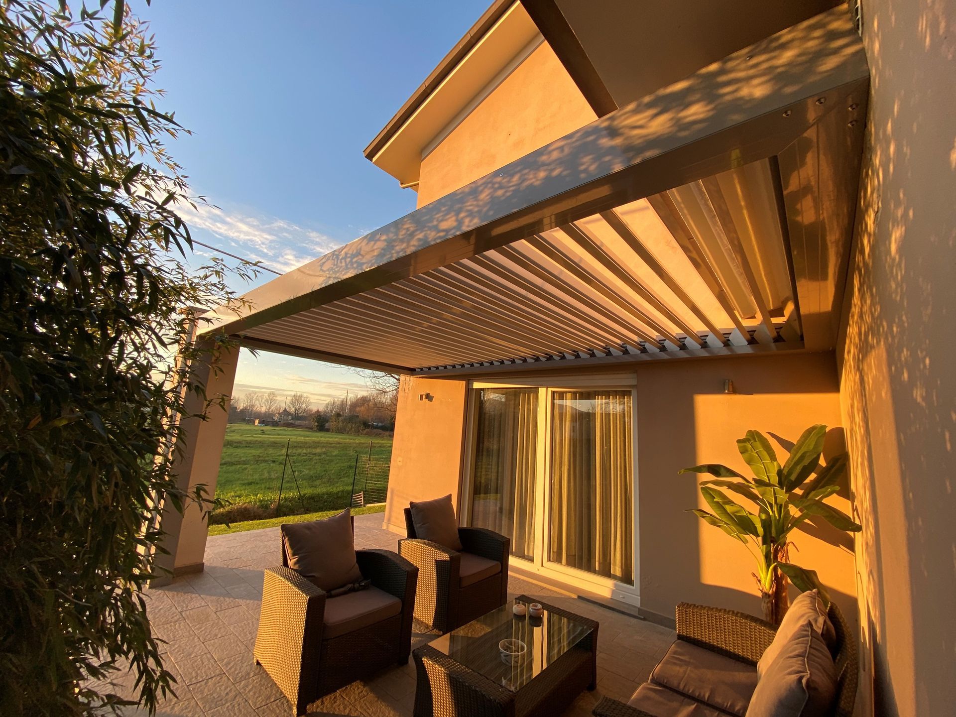 Patio con tetto retrattile e posti a sedere; luce dorata del sole sulla struttura e sulle sedie.