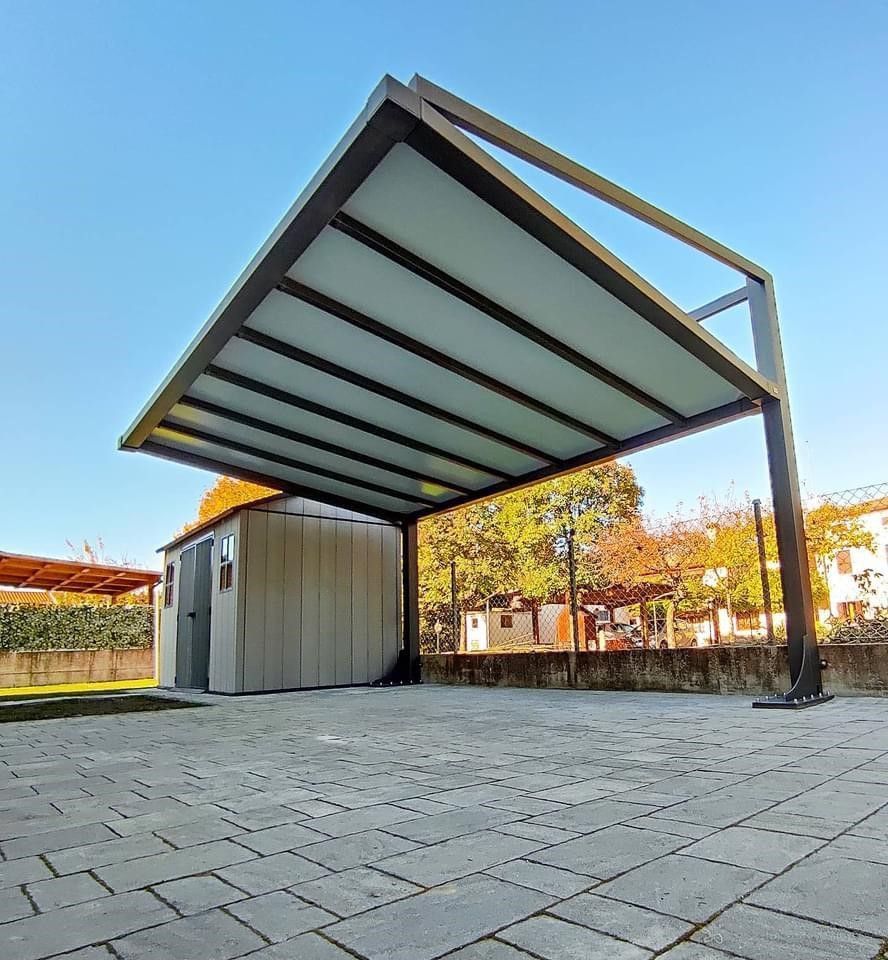 Moderno posto auto coperto con tetto chiaro, sostenuto da travi di metallo scuro, sopra una tettoia su un patio in pietra.