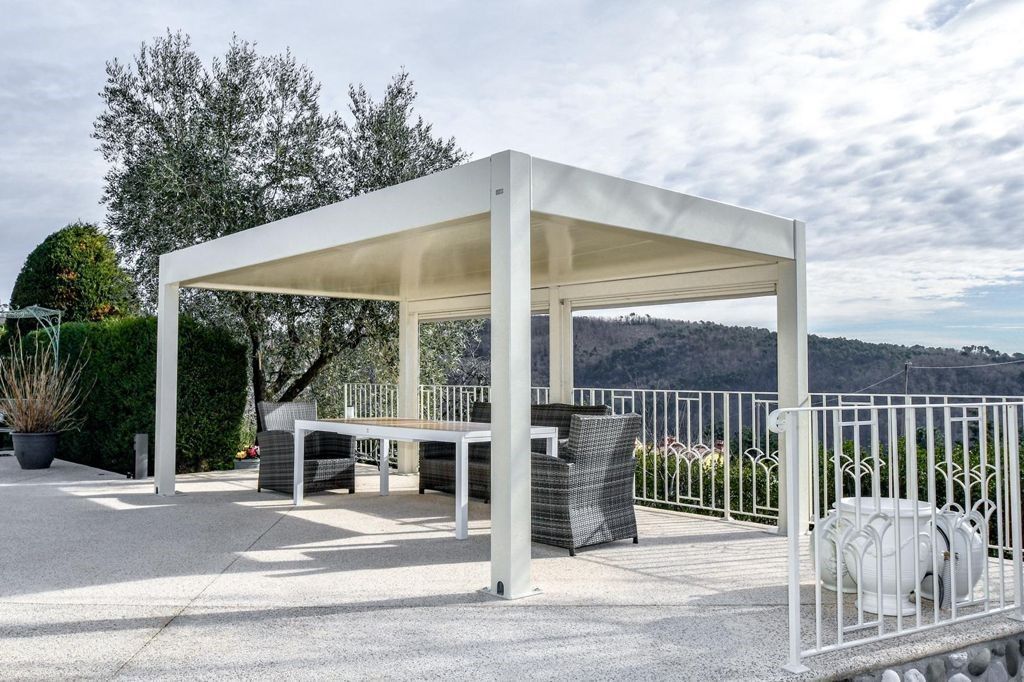 Pergola bianca con tenda da sole color crema sopra un patio con tavolo e sedie, con vista sulla collina.