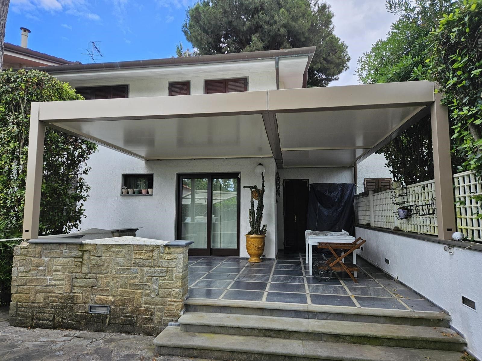 Copertura beige per patio annessa a una casa bianca con patio in pietra scura e gradini.