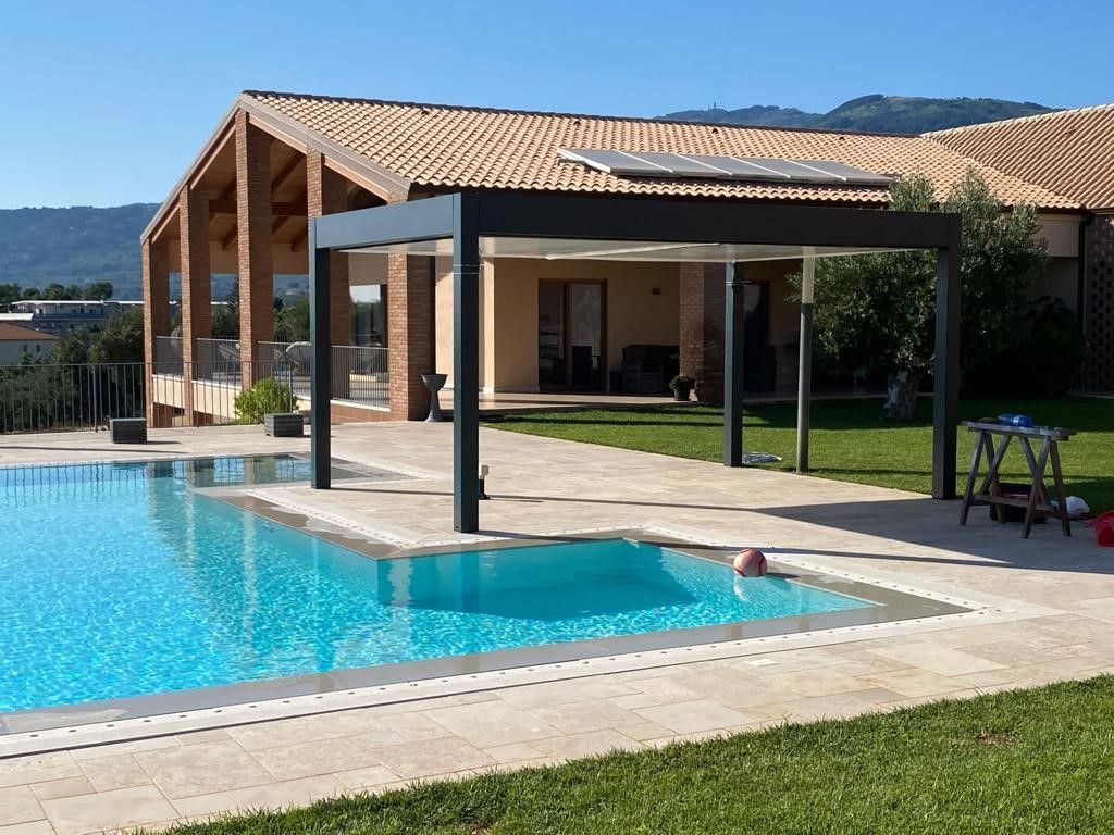 Piscina con pergolato moderno, una casa sullo sfondo ed erba verde.