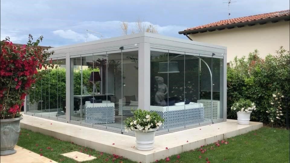 Veranda con vetrate, mobili da esterno, piante in vaso e giardino.