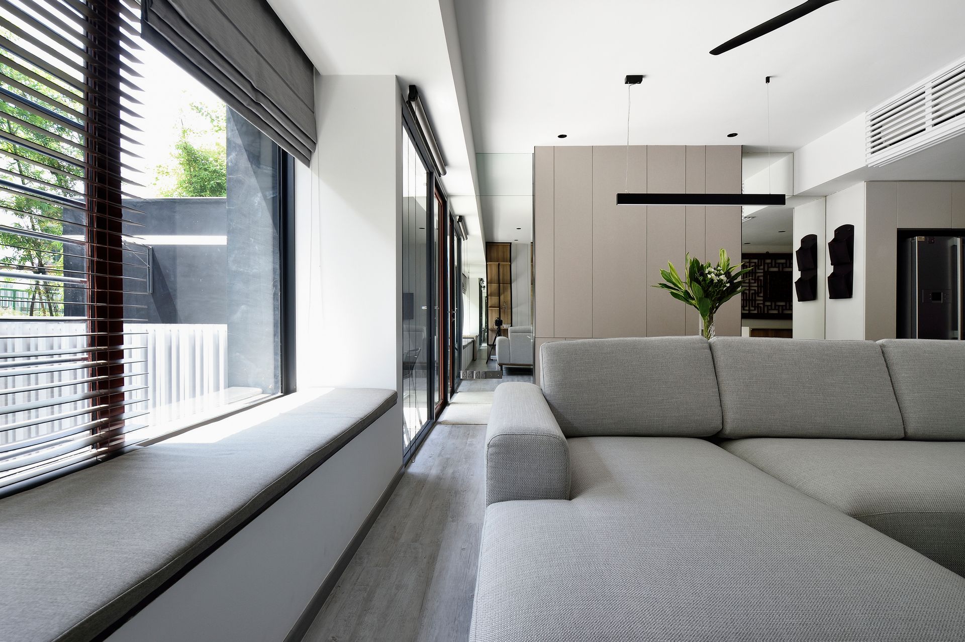 Soggiorno moderno con divano componibile grigio, ampie finestre e palette di colori neutri.